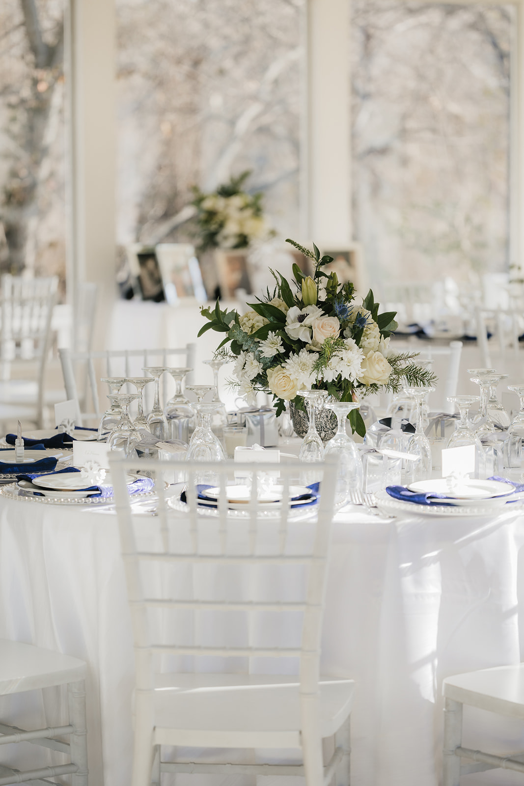 A floral centerpiece on a round table set with white and blue napkins, glassware, and silverware.