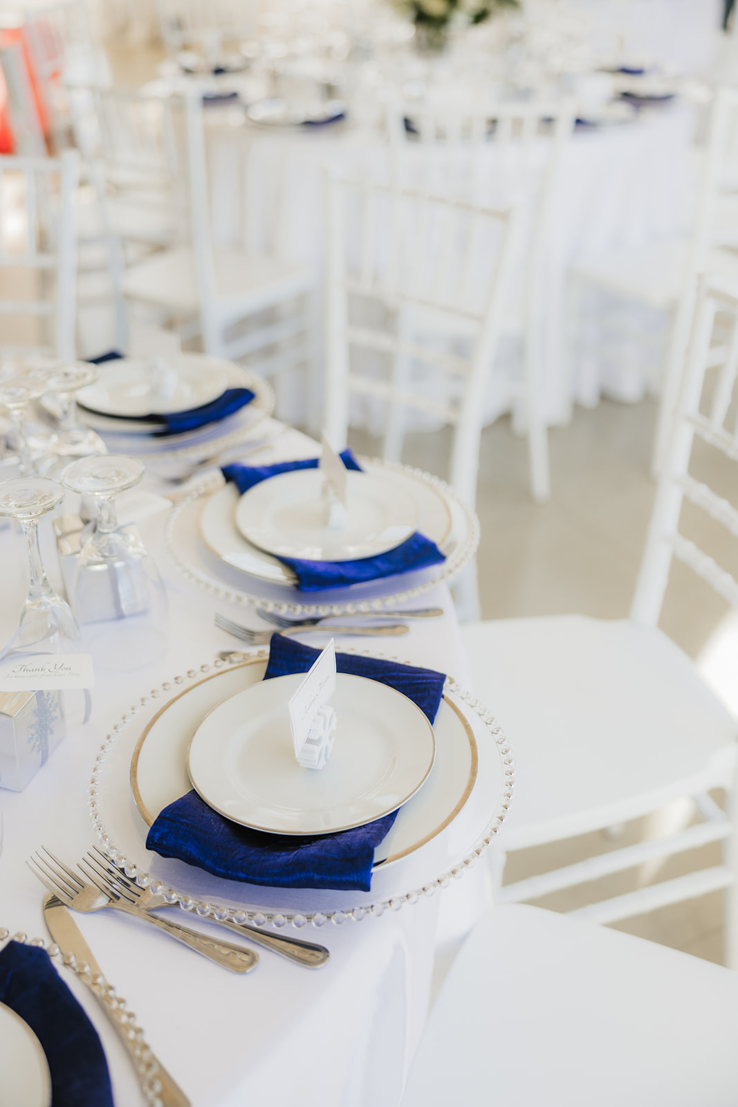 A floral centerpiece on a round table set with white and blue napkins, glassware, and silverware.