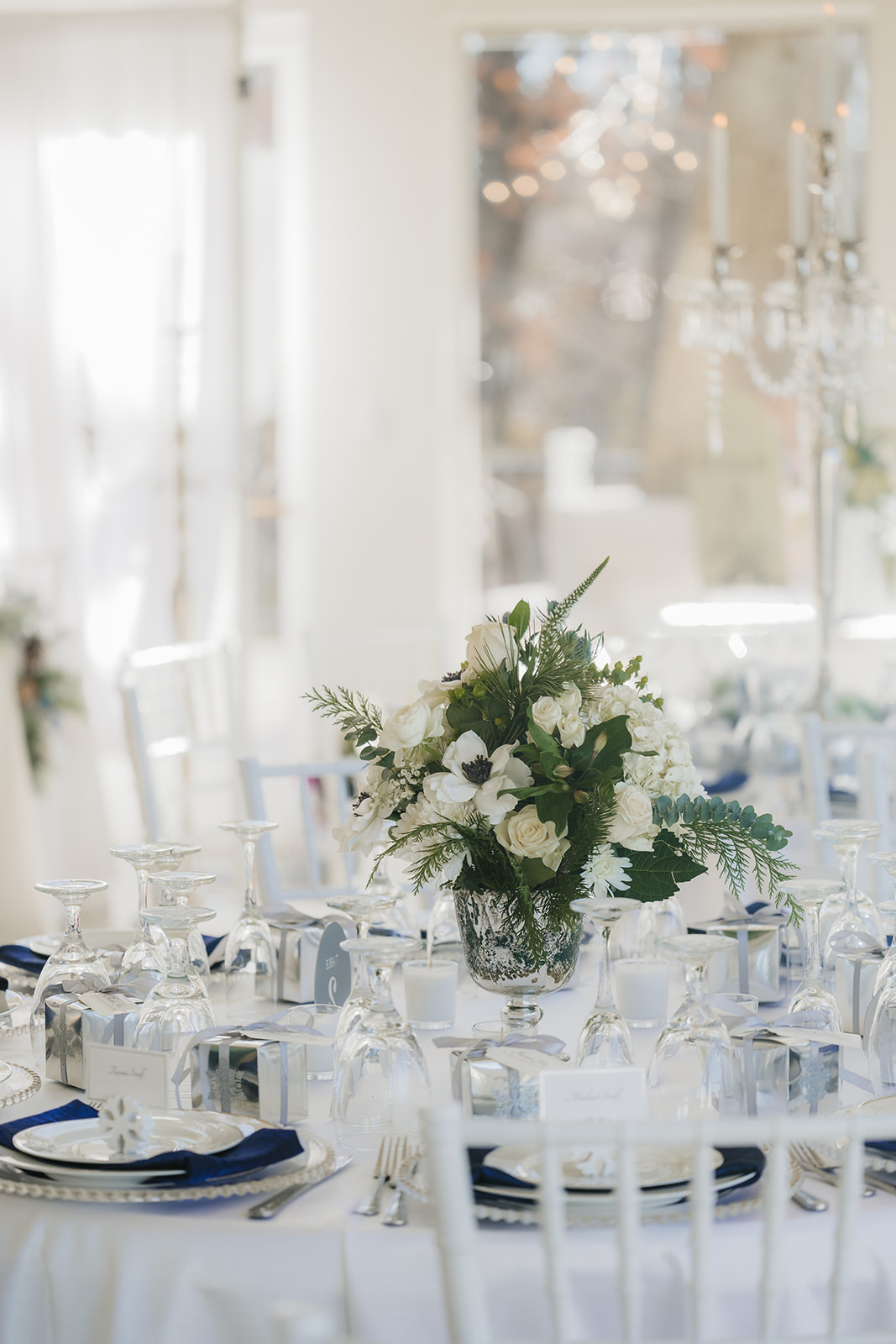 A floral centerpiece on a round table set with white and blue napkins, glassware, and silverware.