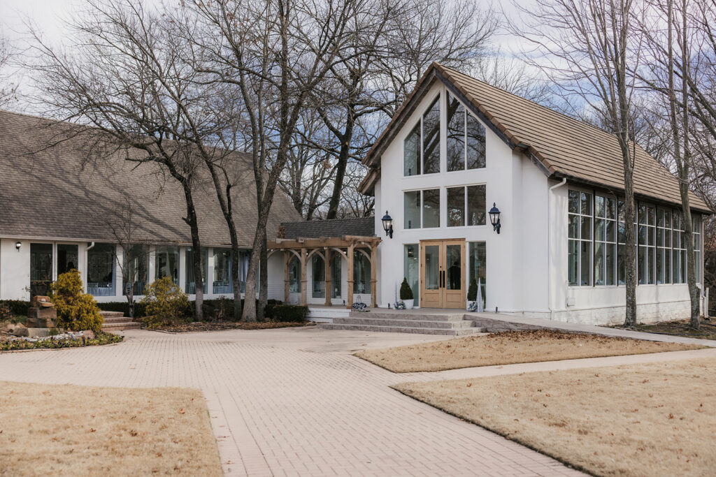 A modern white chapel with large windows and a steep roof, surrounded by leafless trees and a paved walkway.