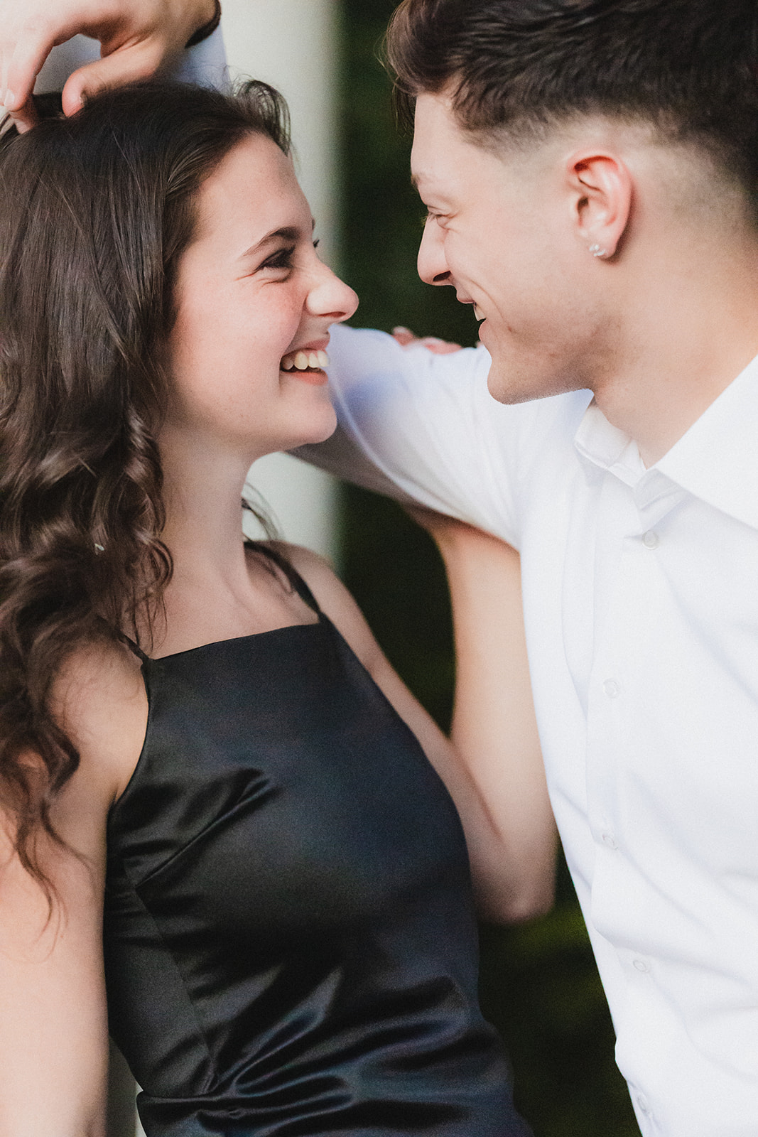 A couple smiles at each other closely, with one person's hand playfully touching the other's hair.