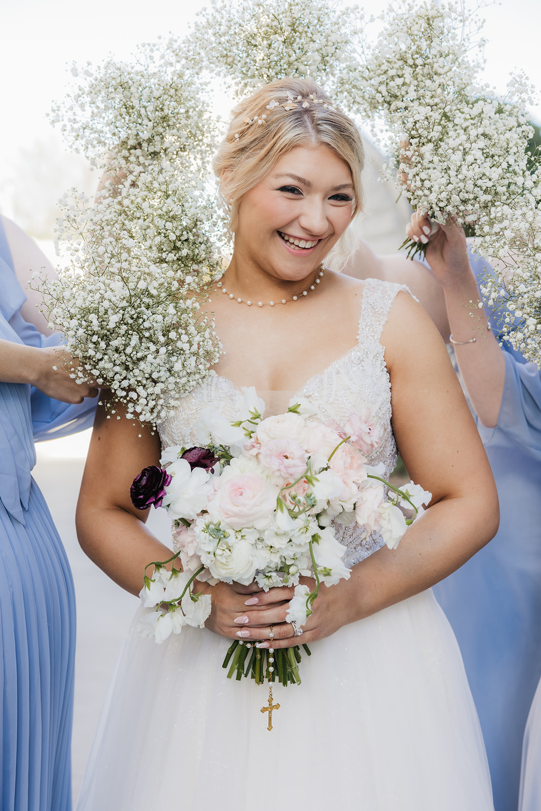 Bride in white dress holding a bouquet of flowers, surrounded by bridesmaids in blue dresses holding baby's breath bouquets.