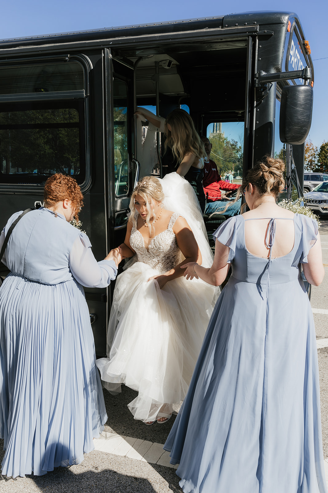 A group of women in matching blue dresses is boarding a black party bus in an urban setting.