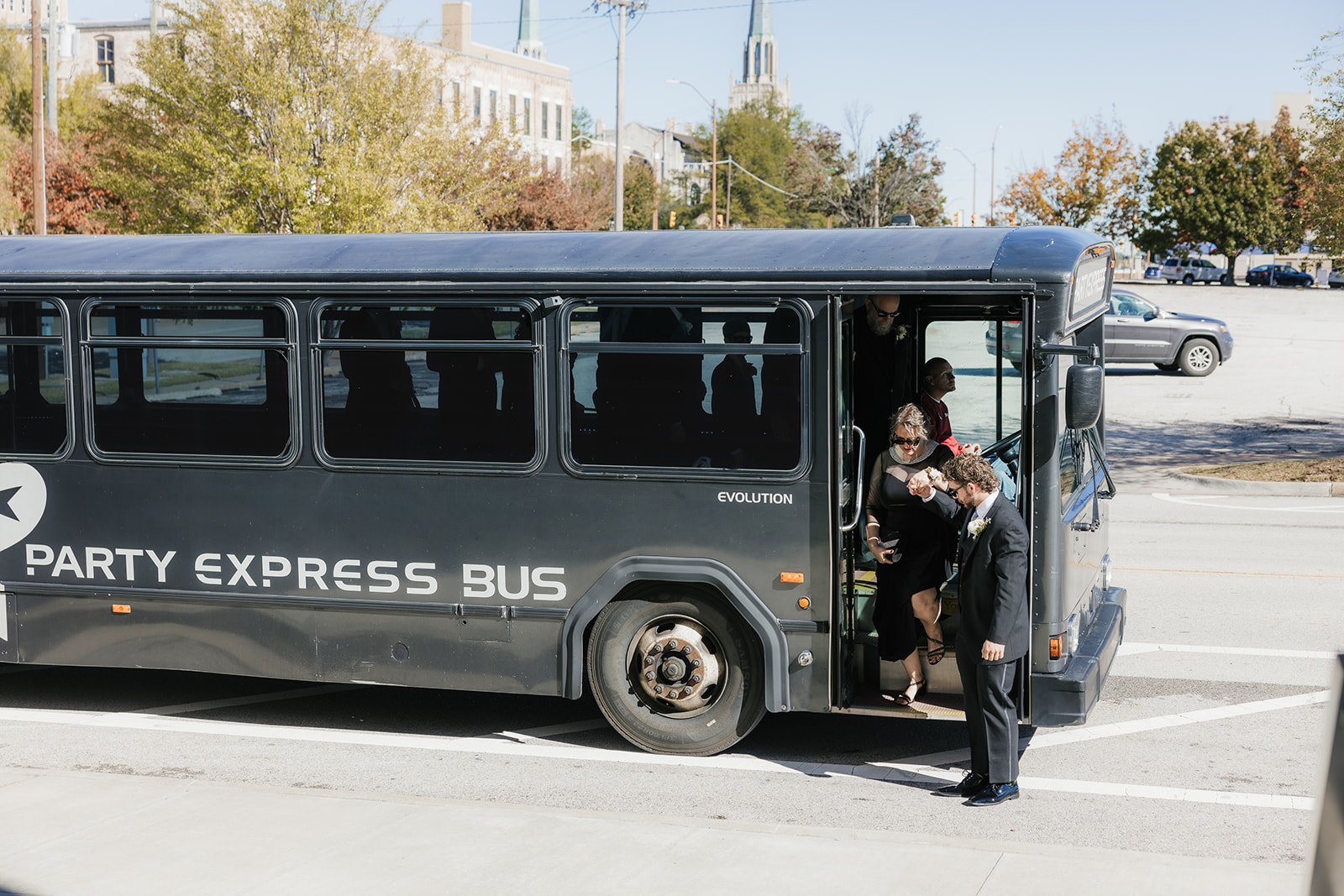 A group of women in matching blue dresses is boarding a black party bus in an urban setting.