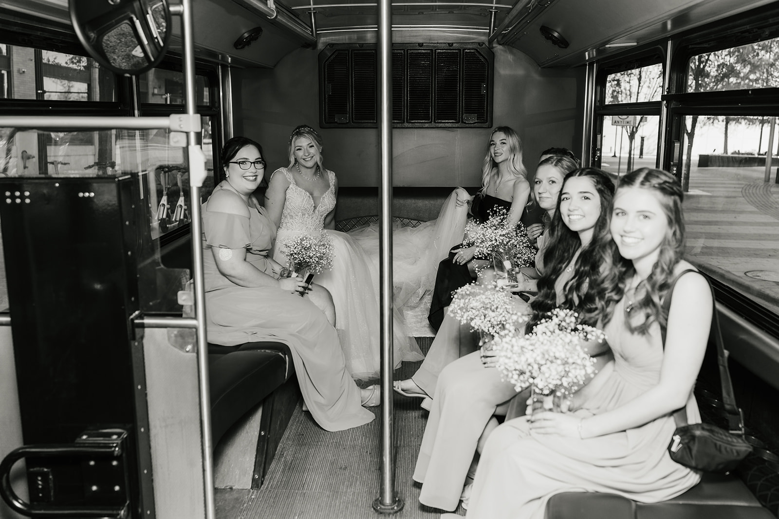 A group of women in matching blue dresses is boarding a black party bus in an urban setting.