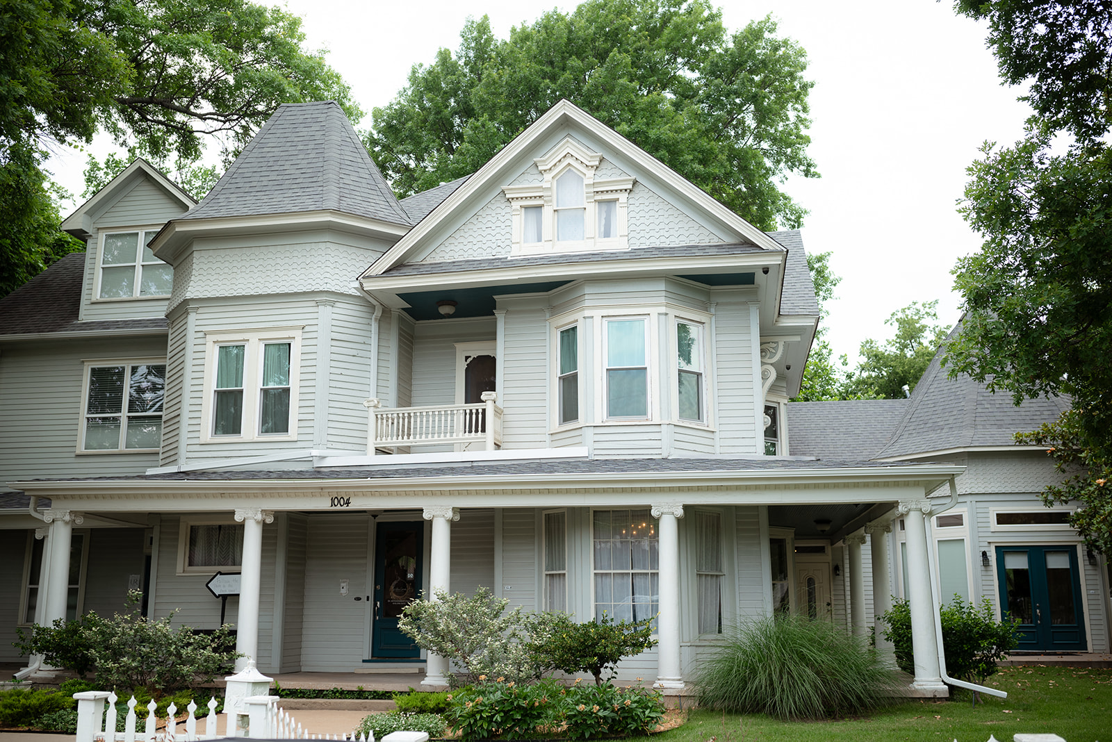 A large, two-story Victorian-style house with a gabled roof, bay windows, and a covered porch, surrounded by greenery and trees.