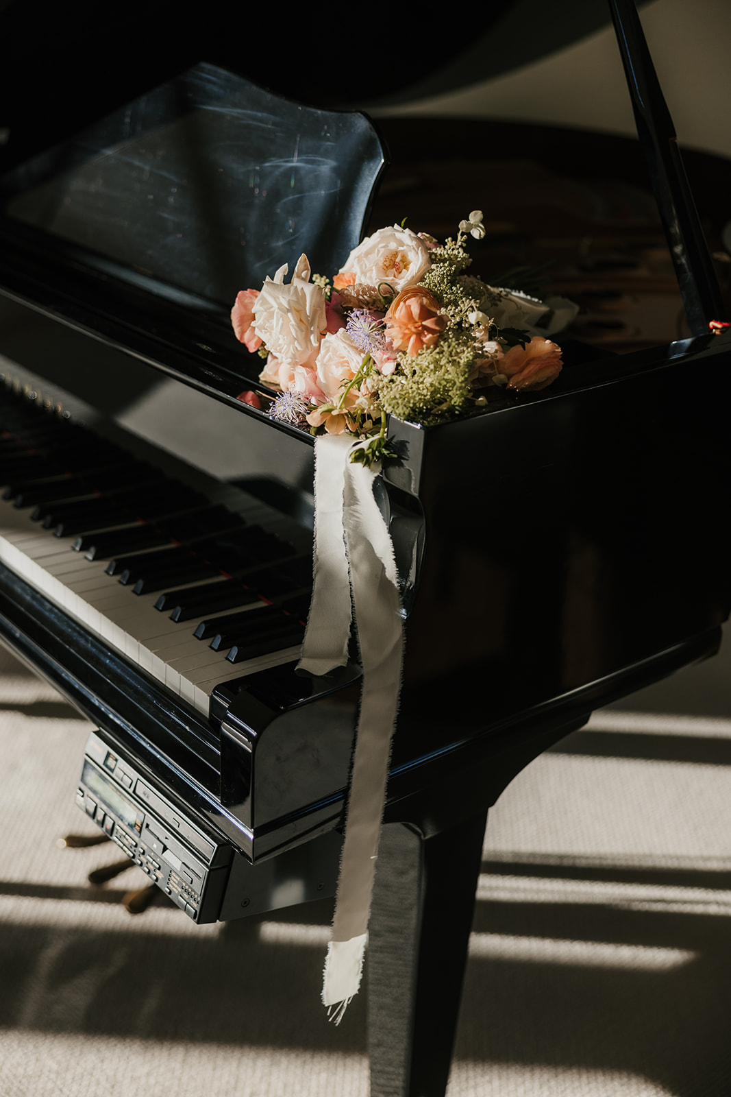 A bouquet of flowers rests on a black grand piano keyboard, with a soft light casting shadows across the scene.