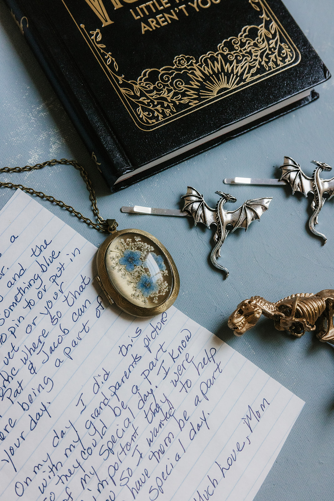 Two enamel pins, one blue and one green, shaped like animals are placed on a silver tray beside yellow wedding invitation cards.