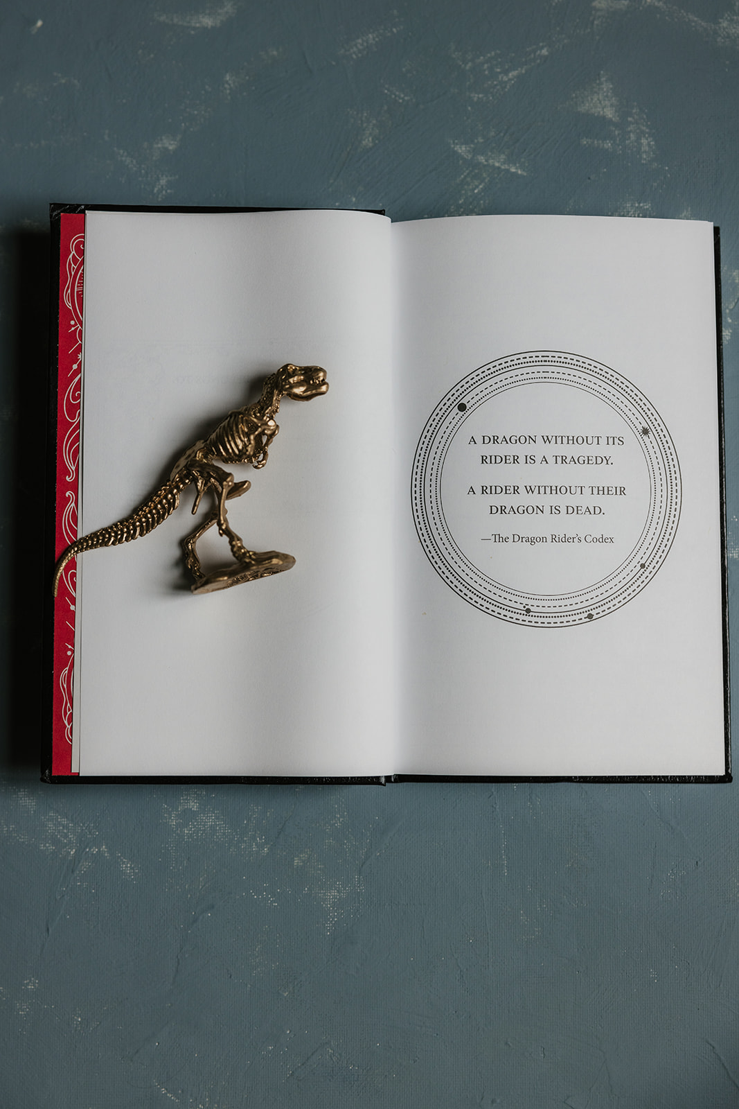 An open book with a small dinosaur figurine placed on the left page and a decorative circular design with text on the right page.