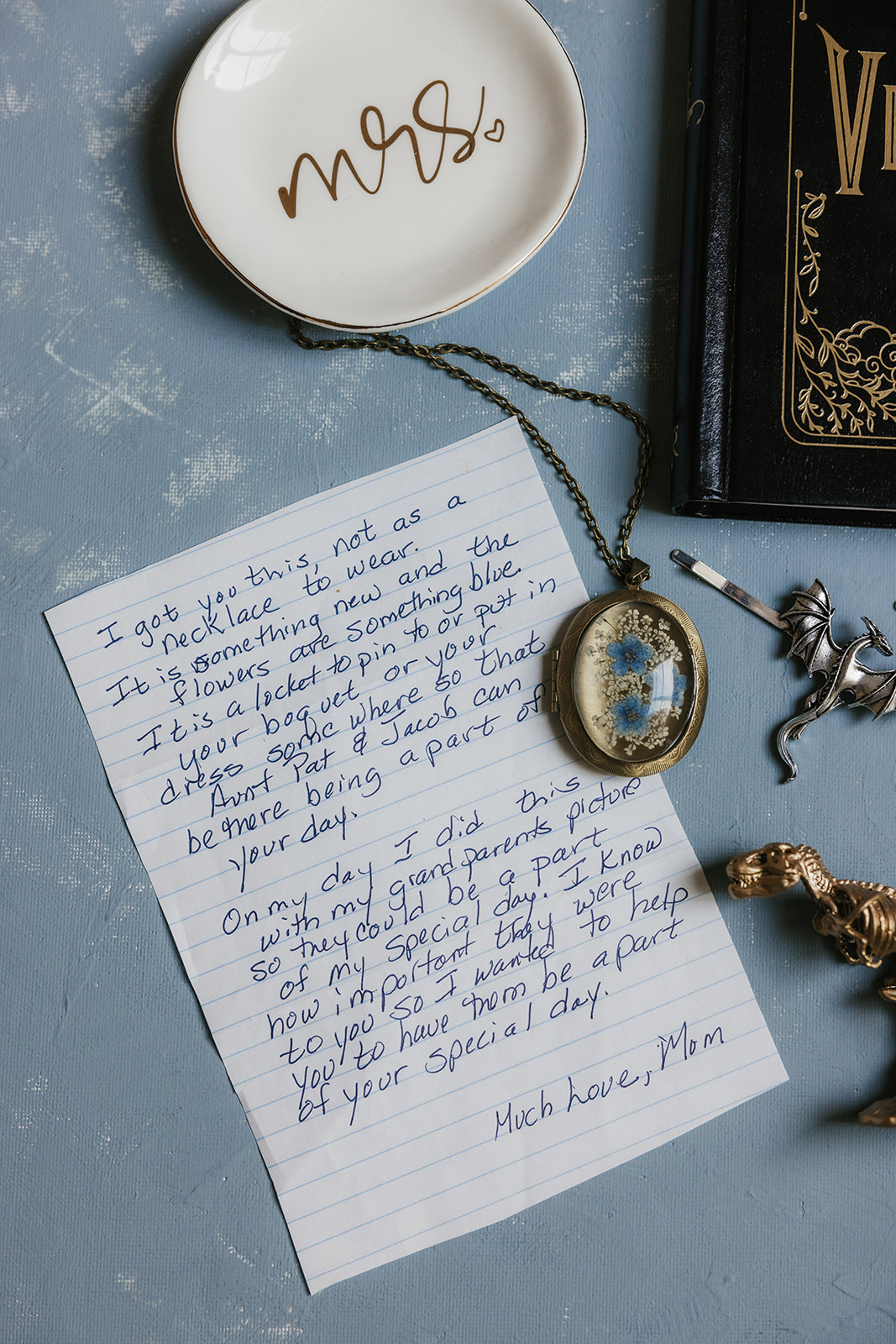 Two enamel pins, one blue and one green, shaped like animals are placed on a silver tray beside yellow wedding invitation cards.
