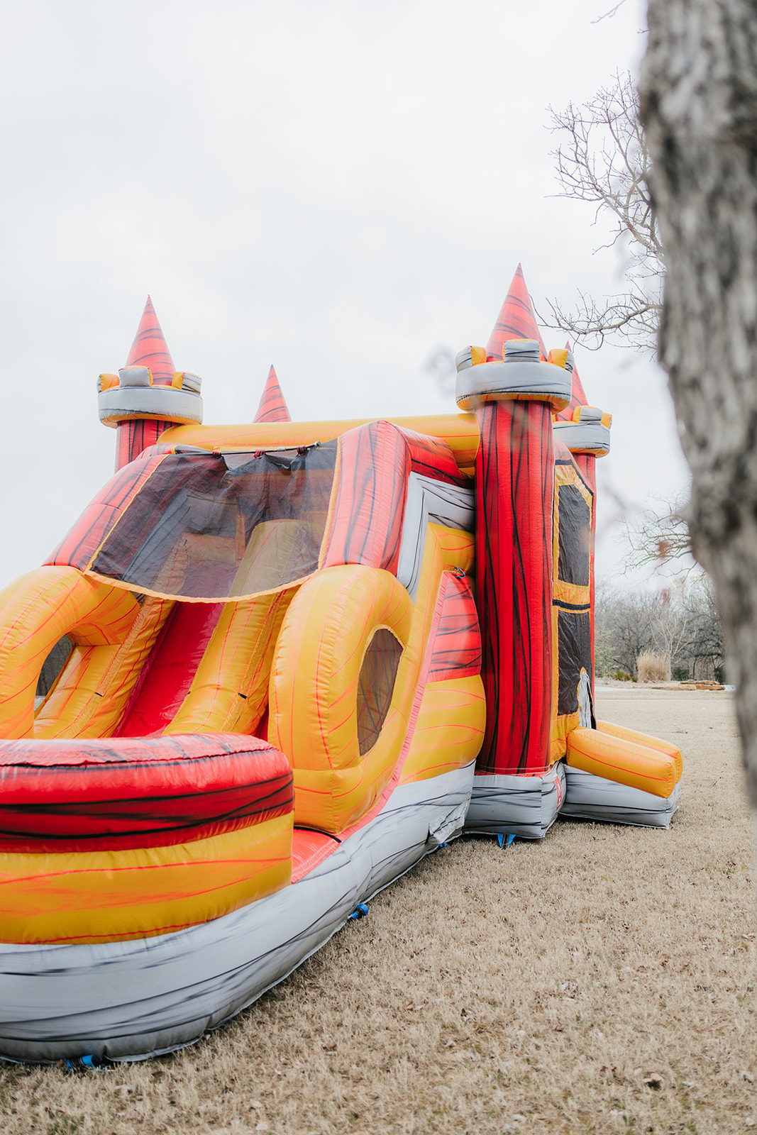 An inflatable bounce house with a slide, designed to look like a red and yellow castle, is set up on a grassy area outdoors.