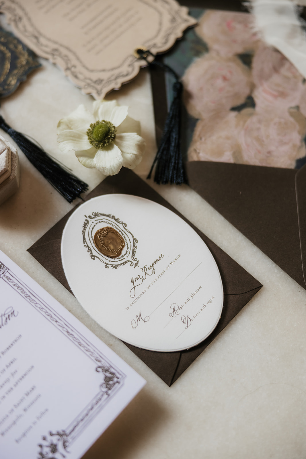 A flat lay of elegant wedding invitations, envelopes, a rosary, a wax seal, and decorative cards arranged on a light surface.