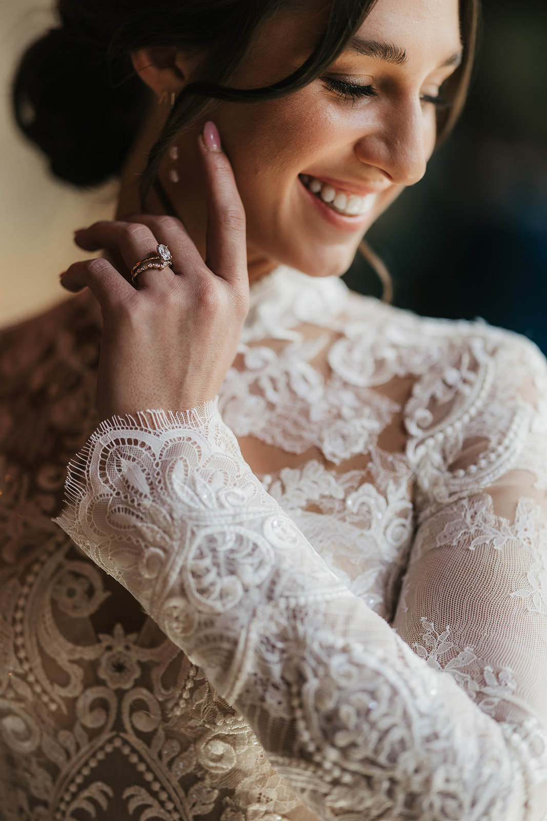 A woman in a white wedding dress stands indoors near a glass door, smiling, with a large classical painting on the wall beside her for catholic wedding ideas