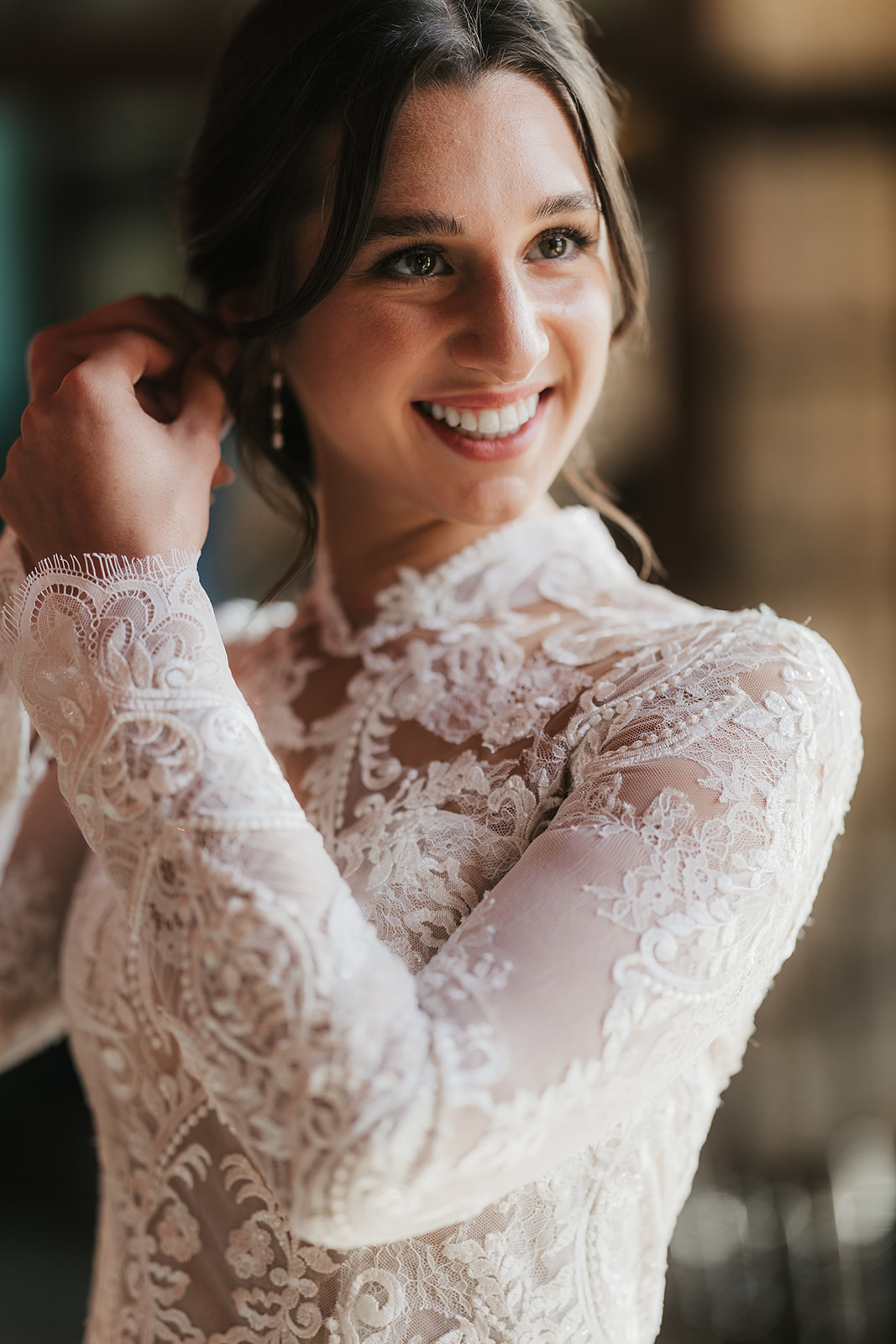 A woman in a white wedding dress stands indoors near a glass door, smiling, with a large classical painting on the wall beside her for catholic wedding ideas