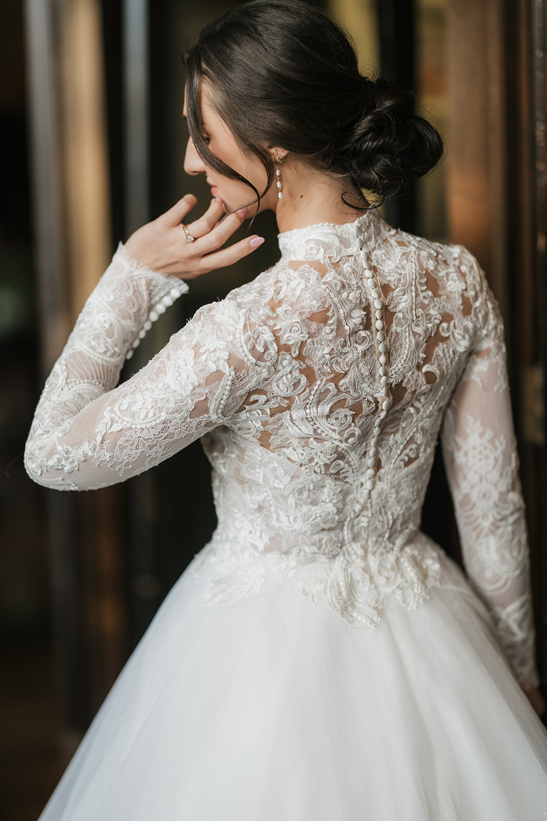 A woman in a white wedding dress stands indoors near a glass door, smiling, with a large classical painting on the wall beside her for catholic wedding ideas