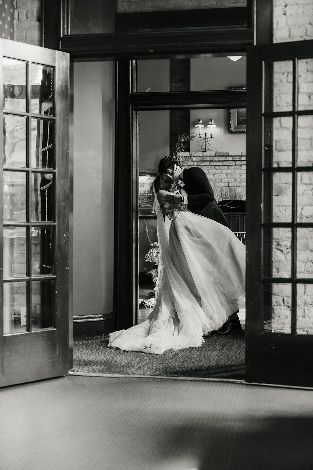 A bride and groom in formal attire hold hands and walk away together in an elegant indoor setting.