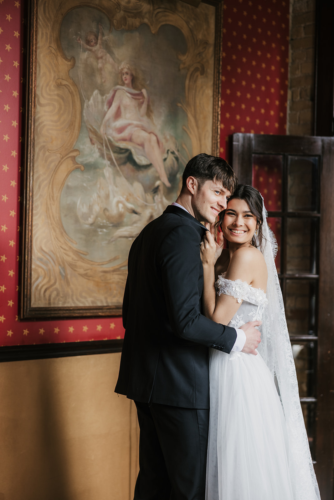 A bride and groom in formal attire hold hands and walk away together in an elegant indoor setting.