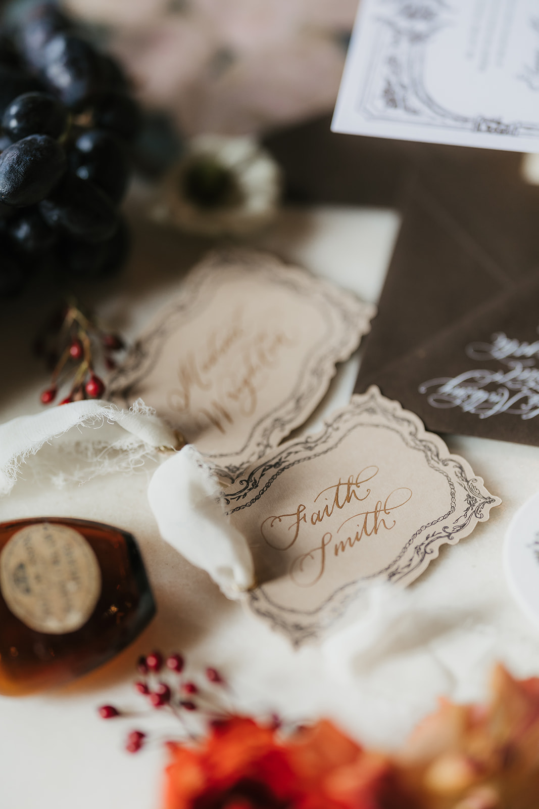 A flat lay of vintage wedding stationery with invitations, envelopes, a rosary, pearls, grapes, wax seal, and decorative flowers arranged on a marble surface for a catholic wedding idea
