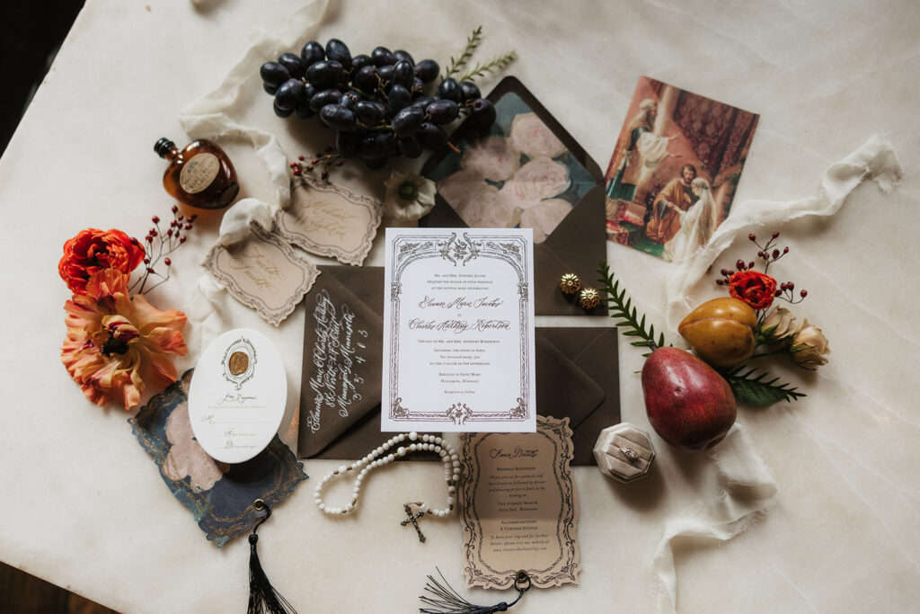 A flat lay of wedding invitations, vintage cards, flowers, fruit, and small decorative items arranged on a light surface.