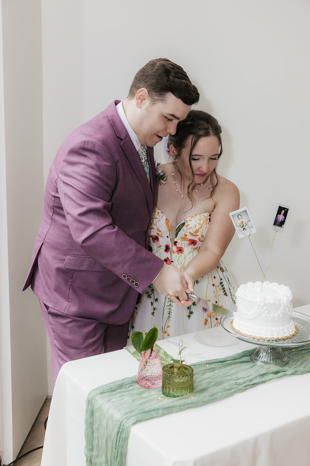 A couple in formal attire cuts a white cake together at a decorated table during a celebration.