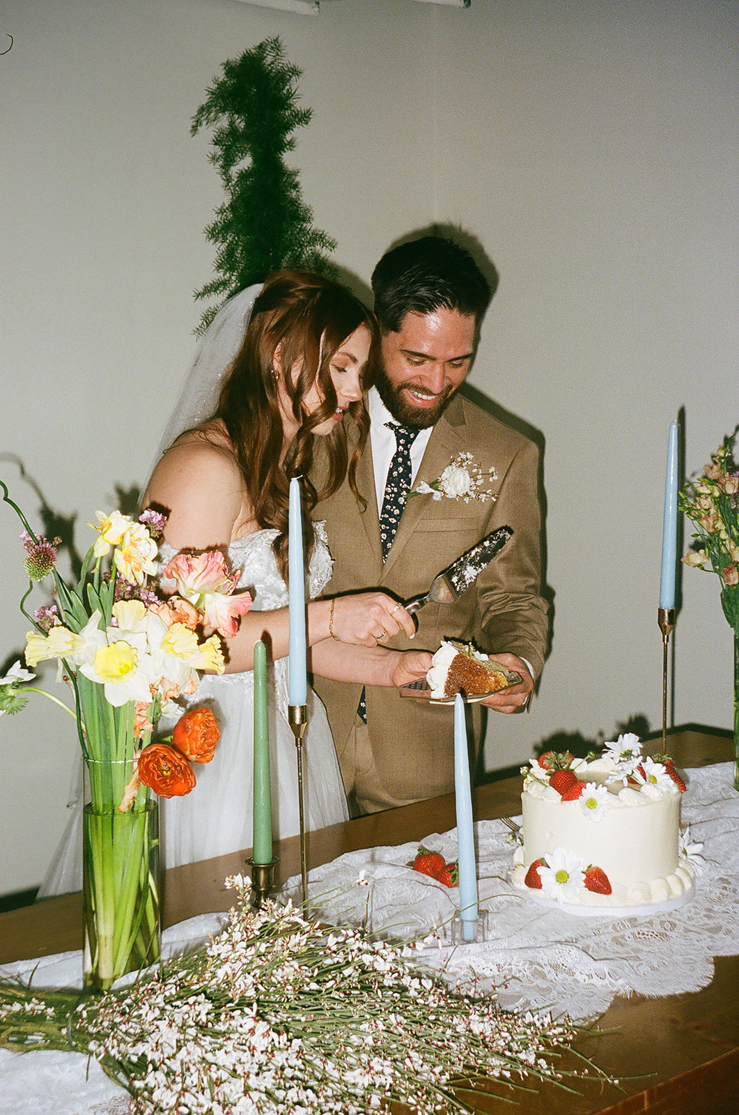 A bride and groom cut a wedding cake together at a decorated table with flowers and candles.