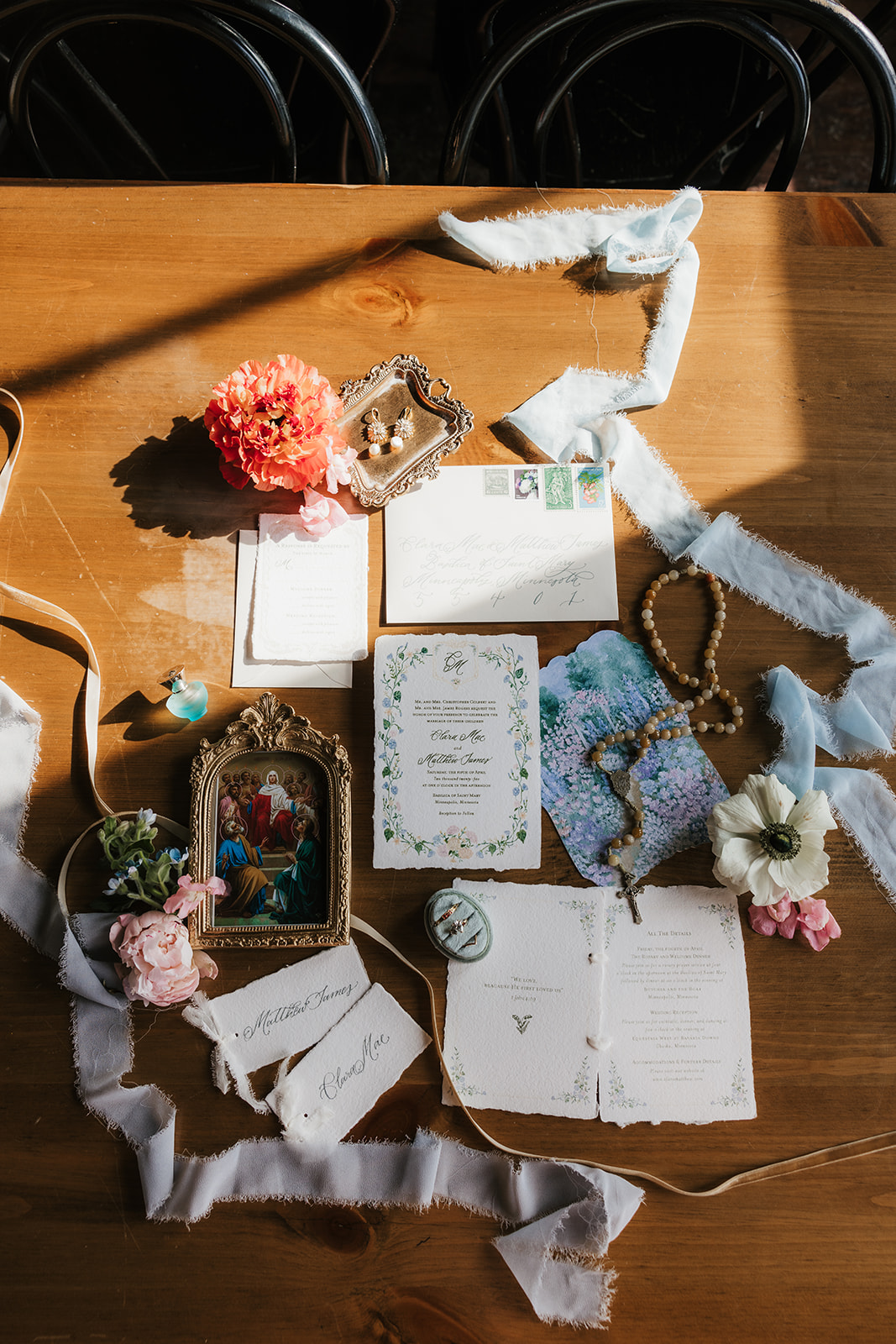 A flat lay of wedding stationery, invitations, vintage frames, ribbon, flowers, and assorted decorative items arranged on a wooden table.