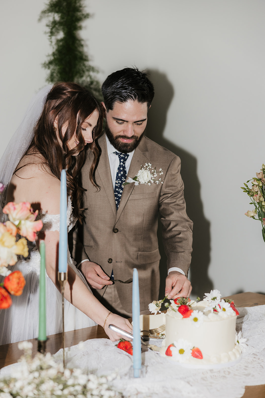 A bride and groom cut a wedding cake together at a decorated table with flowers and candles.