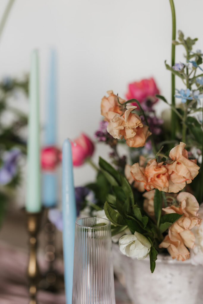 A wooden dining table is set with floral arrangements and candles, with flowers hanging upside down from the ceiling above. Four black chairs surround the table for spring wedding inspo