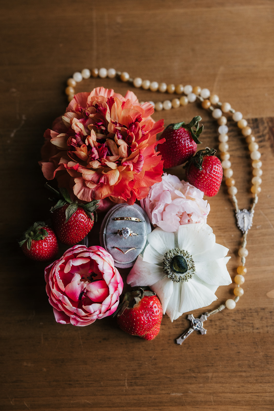 A blue and white decorative plate with strawberries and a porcelain egg, surrounded by flowers, beads, and white fabric on a wooden surface for spring wedding inspo