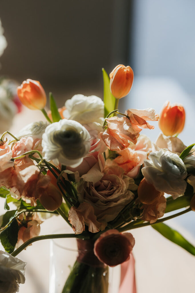 A wooden dining table is set with floral arrangements and candles, with flowers hanging upside down from the ceiling above. Four black chairs surround the table for spring wedding inspo