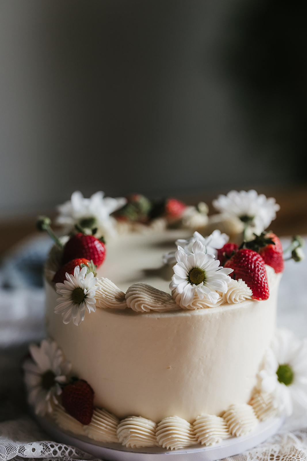 A round cake decorated with white frosting, fresh strawberries, and white flowers on top and around the edges.