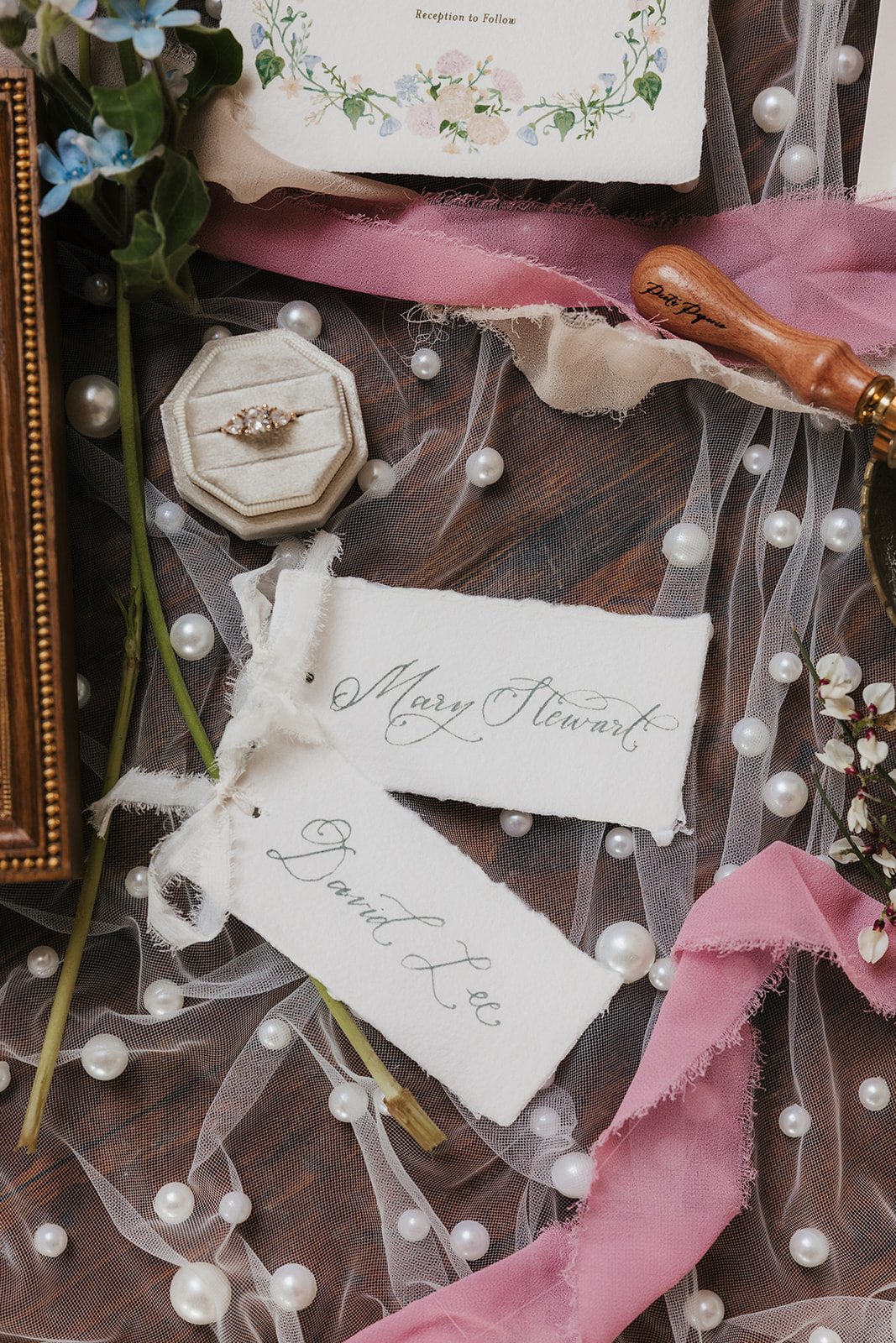 Wedding invitations, stationery, and a religious icon are arranged on a dotted sheer fabric with flowers and ribbons surrounding the items.
