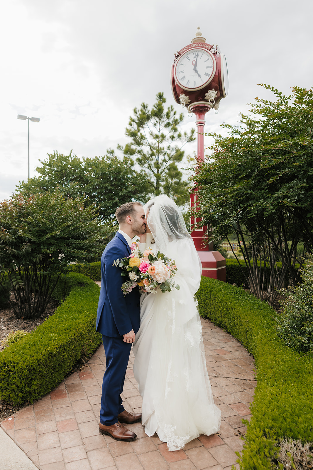 A bride and groom stand in front of a building entrance, sharing a kiss under the bride’s veil outside of St. Thomas More University Parish