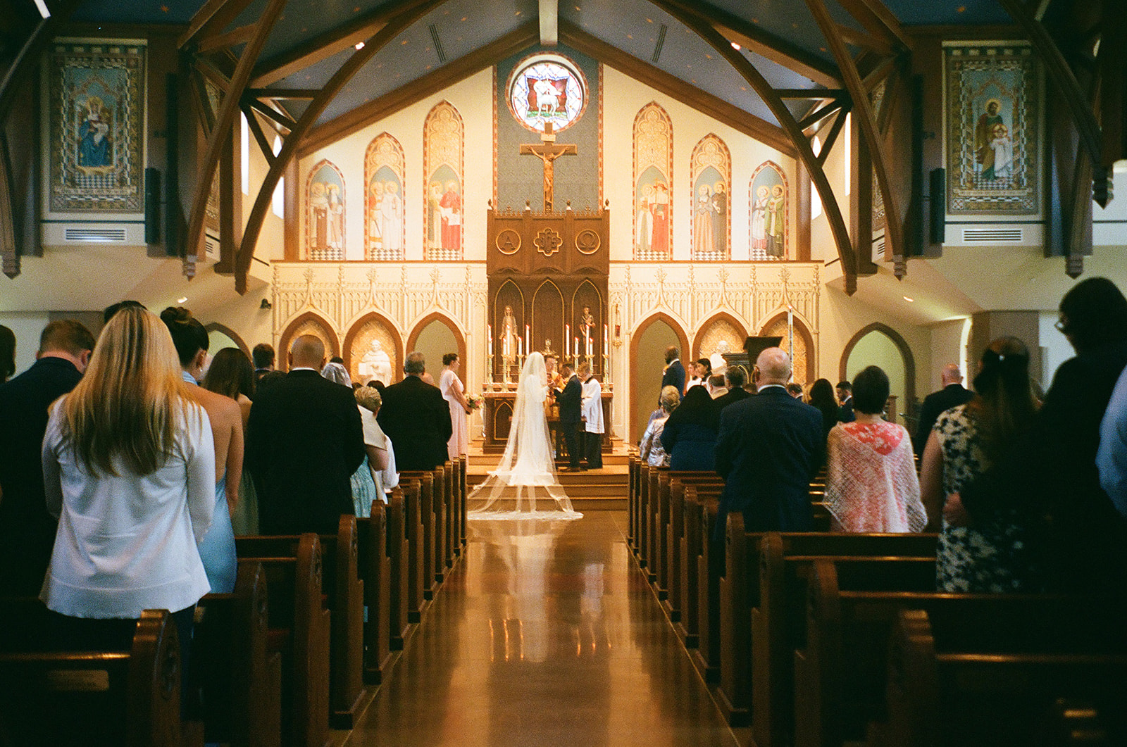 A wedding ceremony takes place at the altar of a church, with guests seated in pews and the couple standing before the officiant.