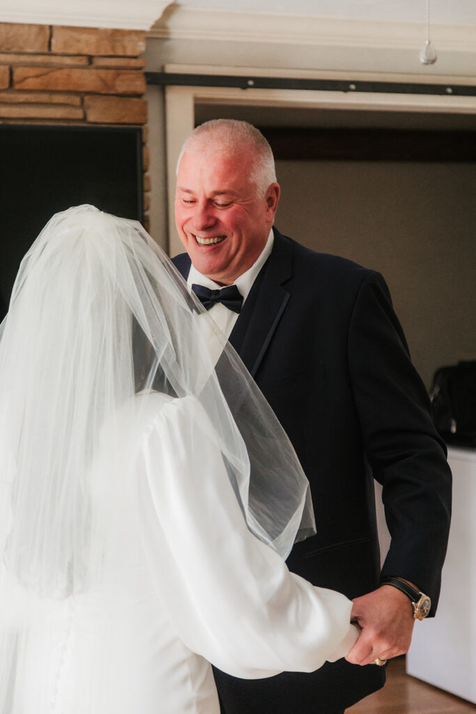 A man in a suit smiles while dancing with a woman in a white wedding dress and veil indoors for a wedding at St. Thomas More University Parish