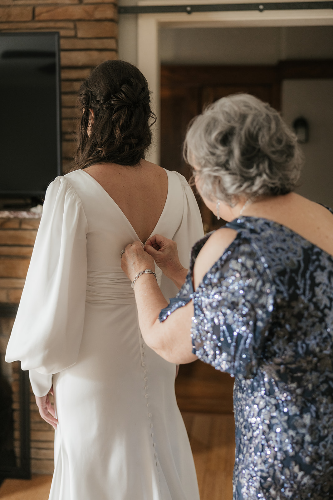 A bride in a white dress stands indoors, holding hands with two women in formal dresses, preparing for a wedding at St. Thomas More University Parish