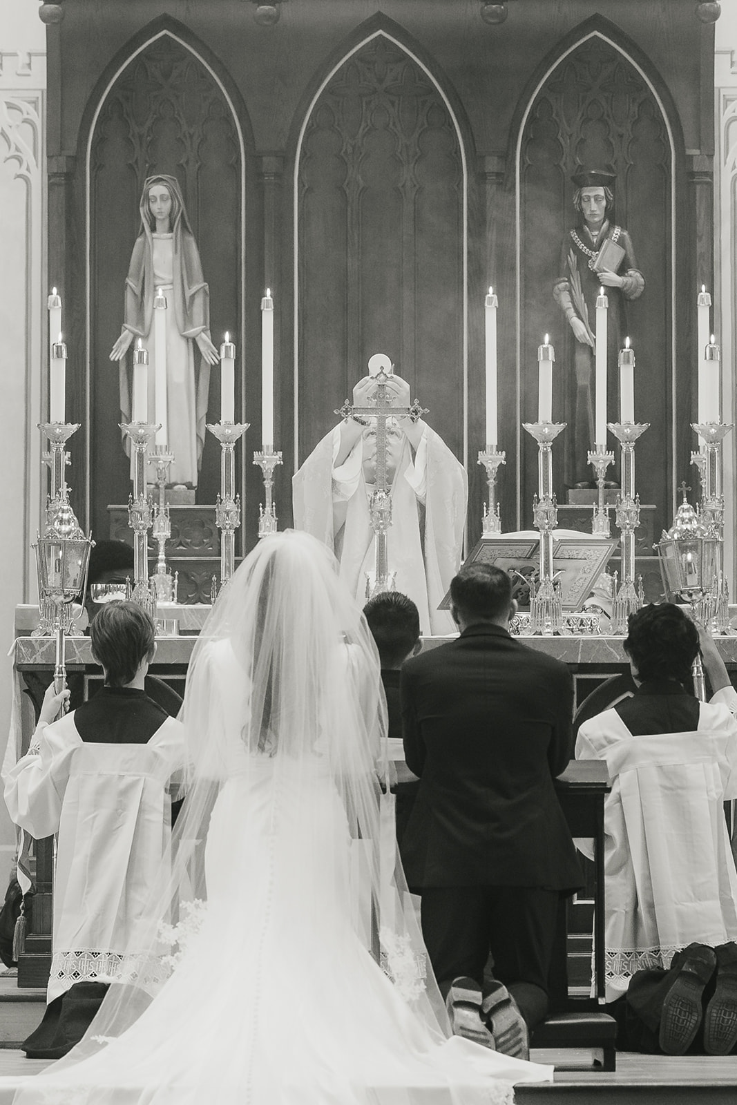 A bride walks down the aisle of a church filled with seated and standing guests, viewed from above in black and white.
