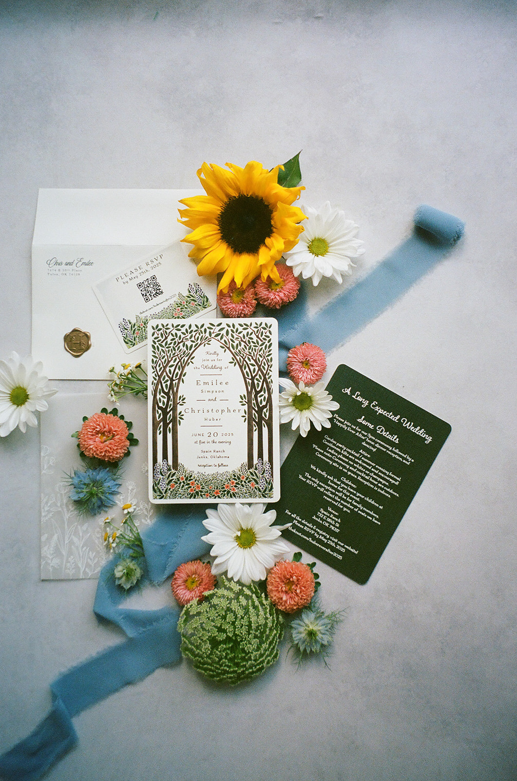A decorative card with a tree design sits on a silver tray surrounded by assorted flowers, including a sunflower, daisies, and pink blooms.