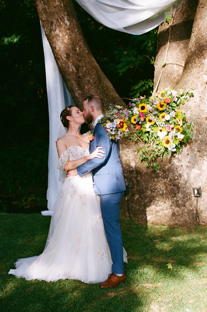A bride and groom stand at an outdoor altar under trees, exchanging vows in front of seated guests on a sunny day for an outdoor wedding ceremony at  spain ranch