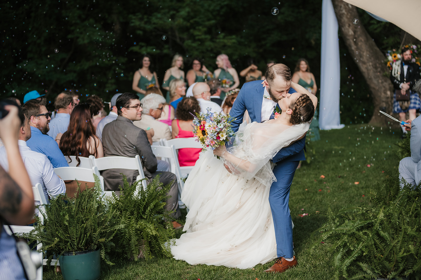  A bride and groom kiss as the groom dips the bride in front of seated wedding guests at an outdoor ceremony.