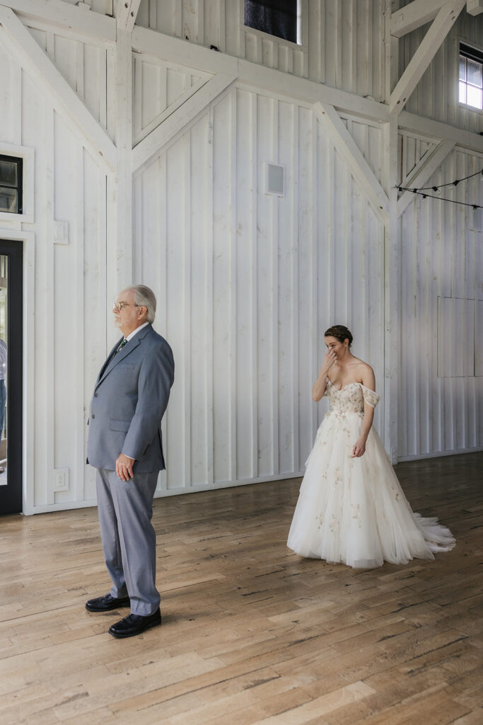 A man in a suit reads from a card while standing across from a woman in a wedding dress inside a bright, wooden-paneled room.