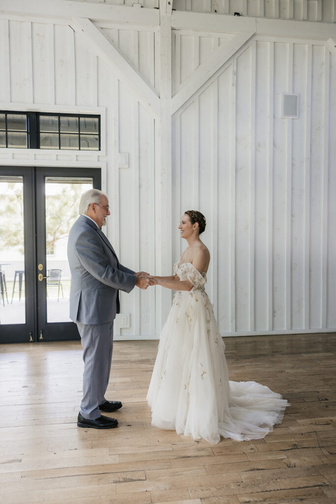 A man in a suit reads from a card while standing across from a woman in a wedding dress inside a bright, wooden-paneled room.