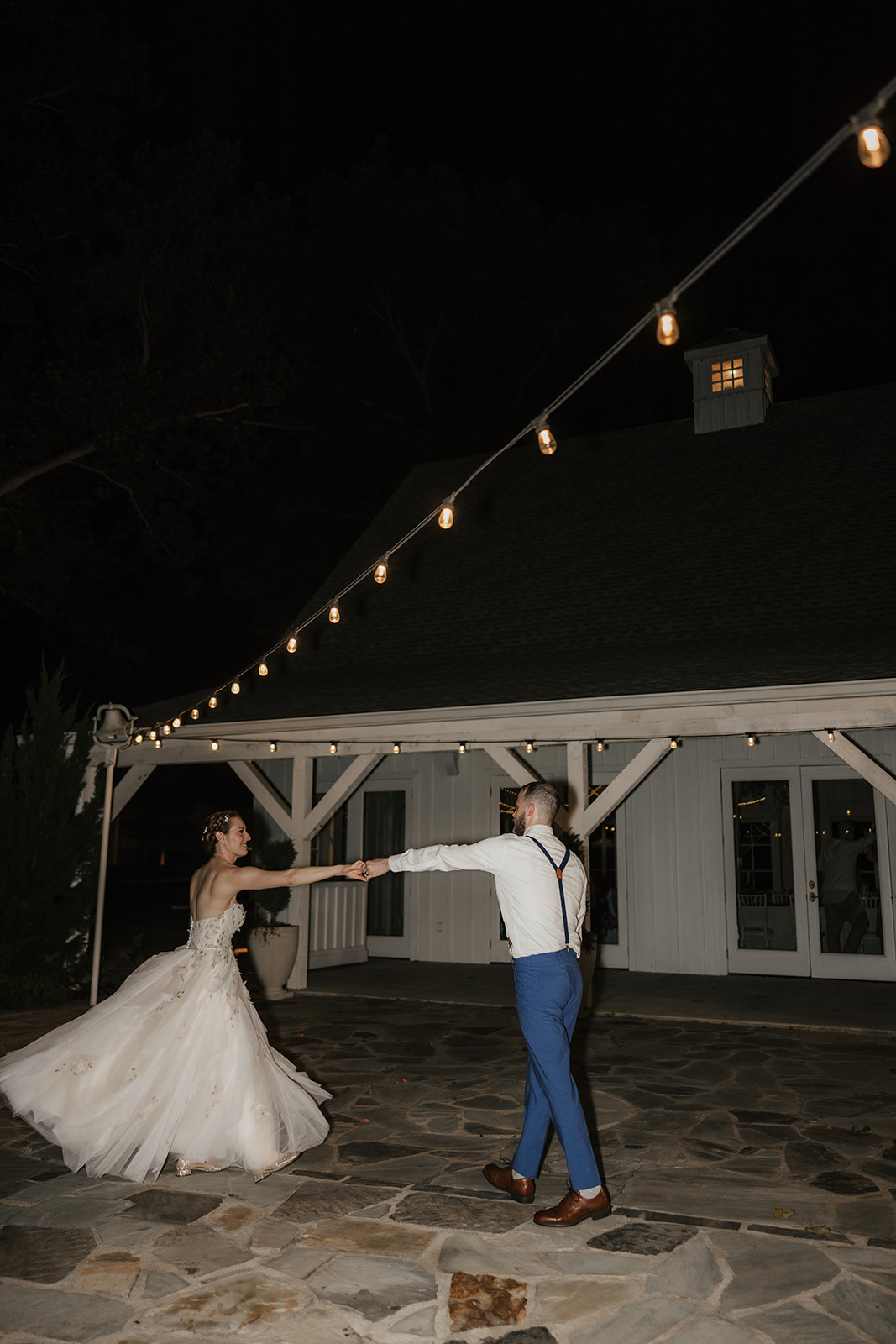 A bride and groom dance together outdoors at night, dressed in formal wedding attire.