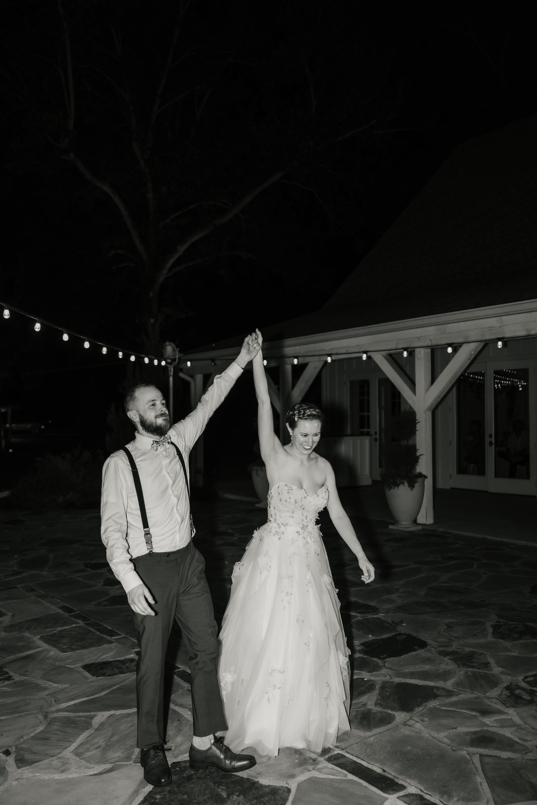 A bride and groom dance together outdoors at night, dressed in formal wedding attire.