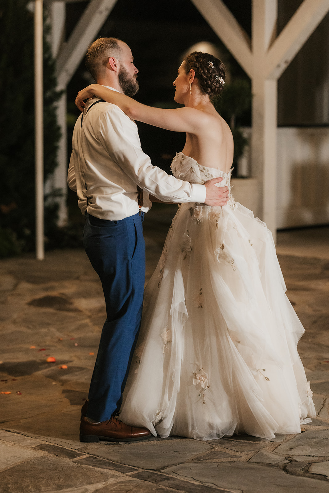 A bride and groom dance together outdoors at night, dressed in formal wedding attire.