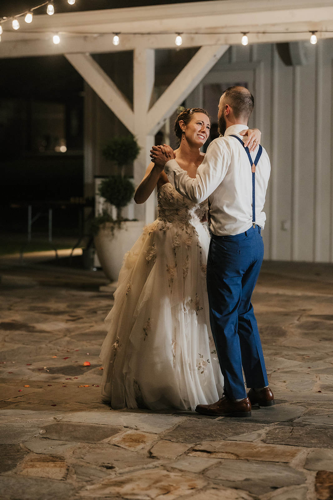 A bride and groom dance together outdoors at night, dressed in formal wedding attire.