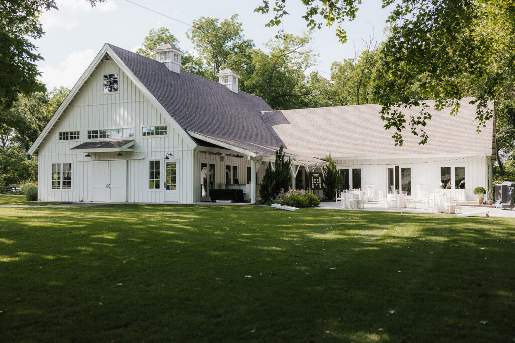 Single-story white house with a large, sloped roof, surrounded by trees and greenery, with a curved driveway in front.
