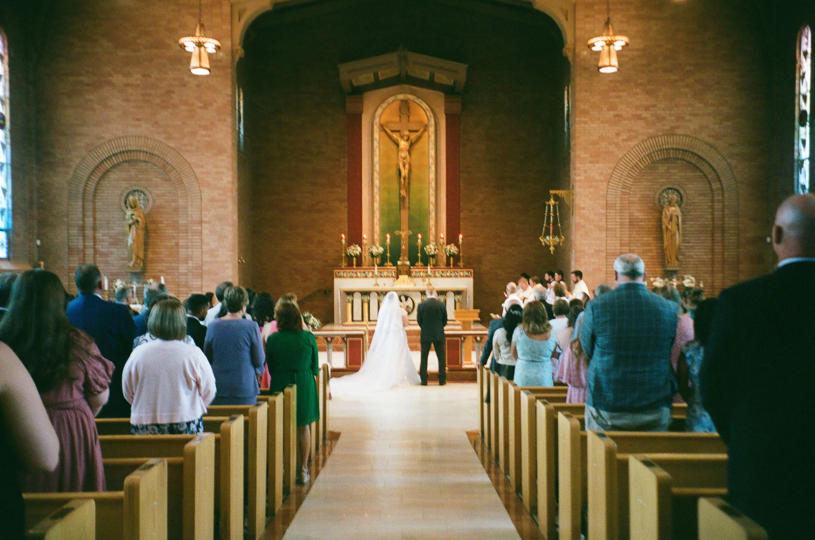 A bride and groom stand at the altar during a wedding ceremony in a church, with guests seated in pews observing.