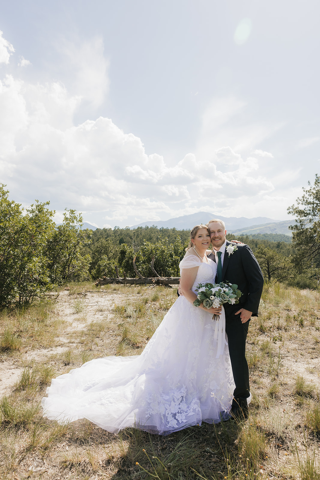 catholic wedding photos of A bride and groom stand outdoors in wedding attire, facing each other under a veil, surrounded by greenery and a cloudy sky for catholic wedding photos