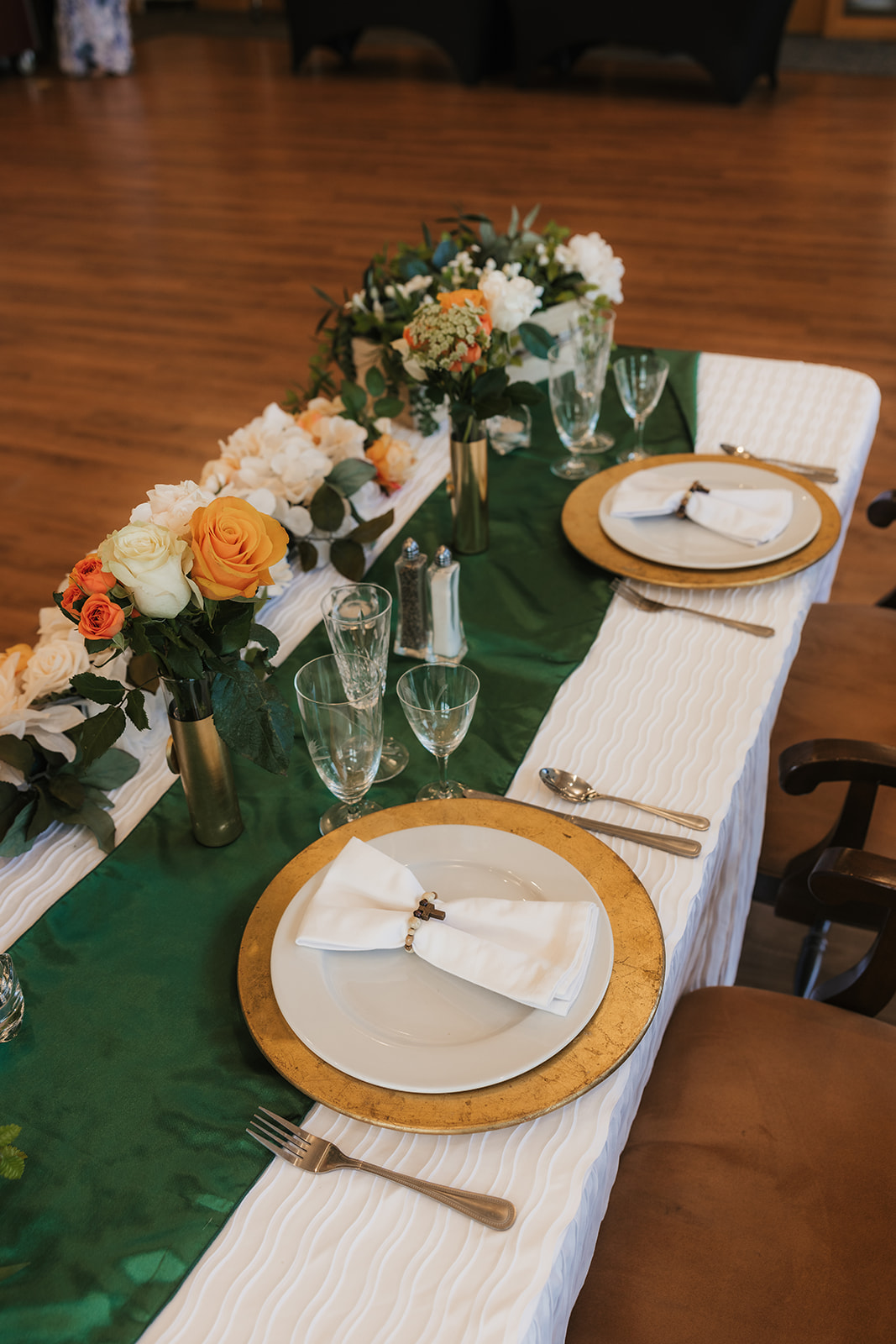 A decorated table with flowers and greenery is set in front of two chairs, positioned by large windows and glass doors in a bright indoor space.